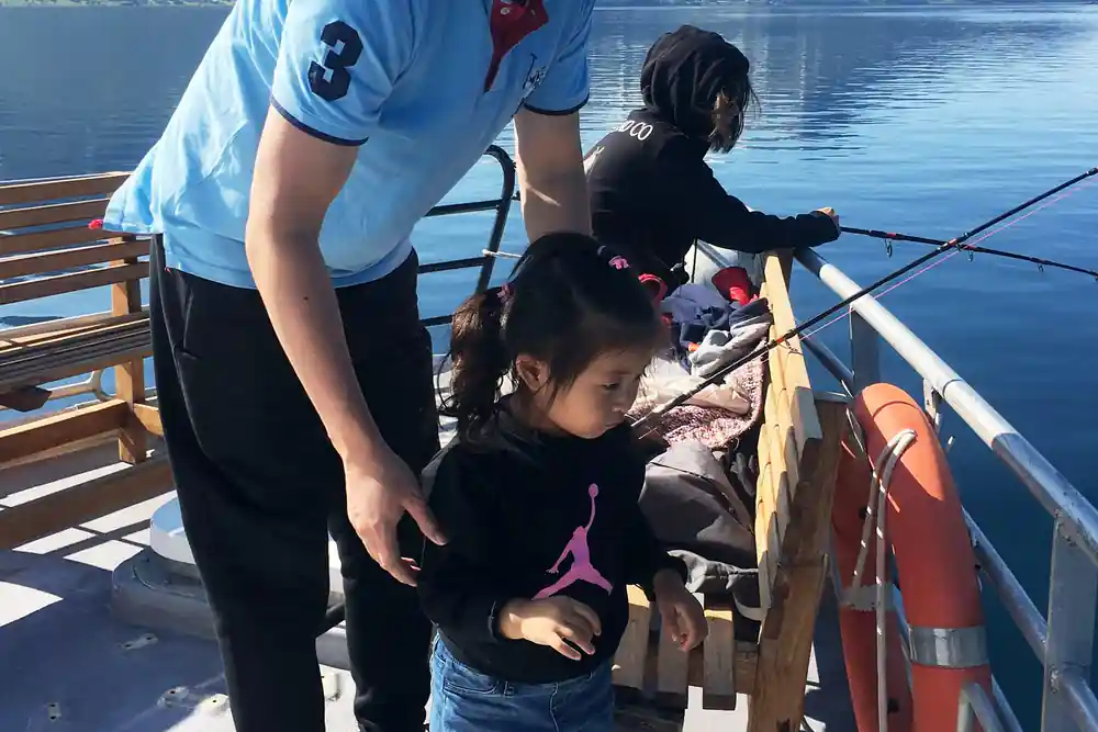 Child and adults fishing from boat railing