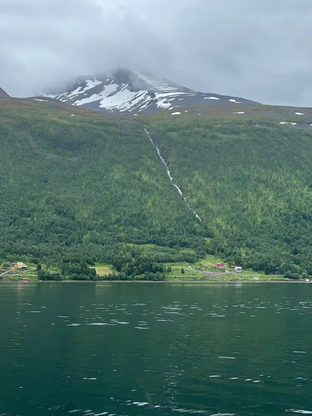 Green forested mountainside with waterfall and lake