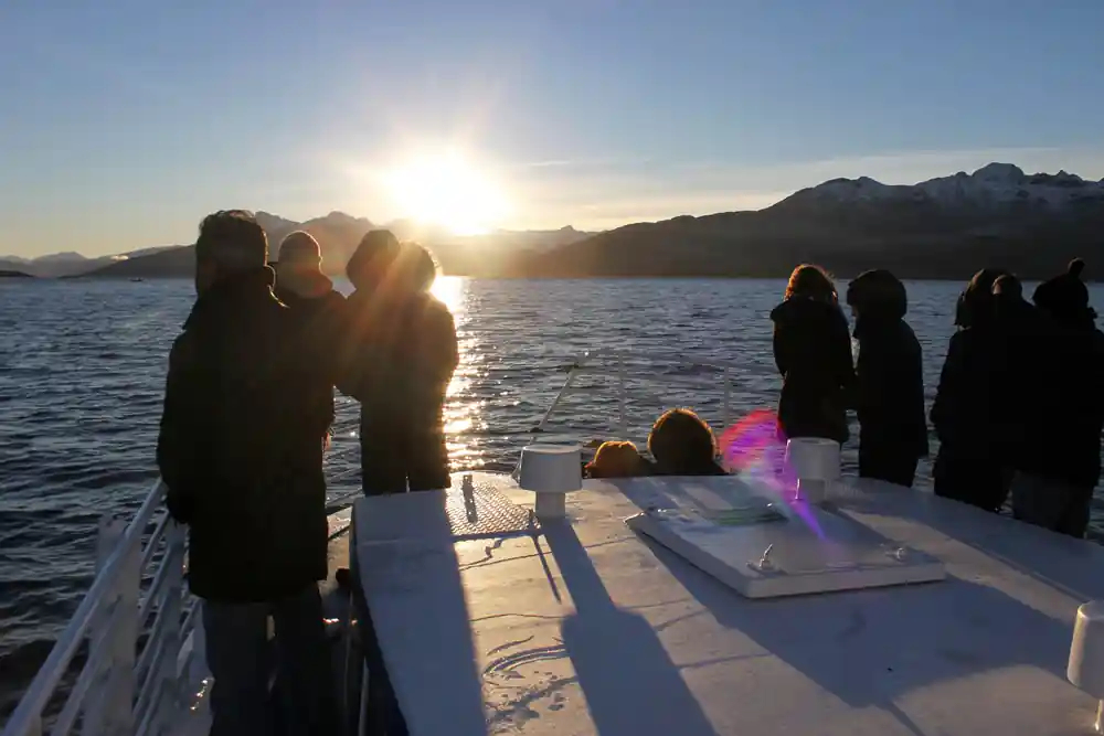 Group of people on boat at sunrise with snow-capped mountains