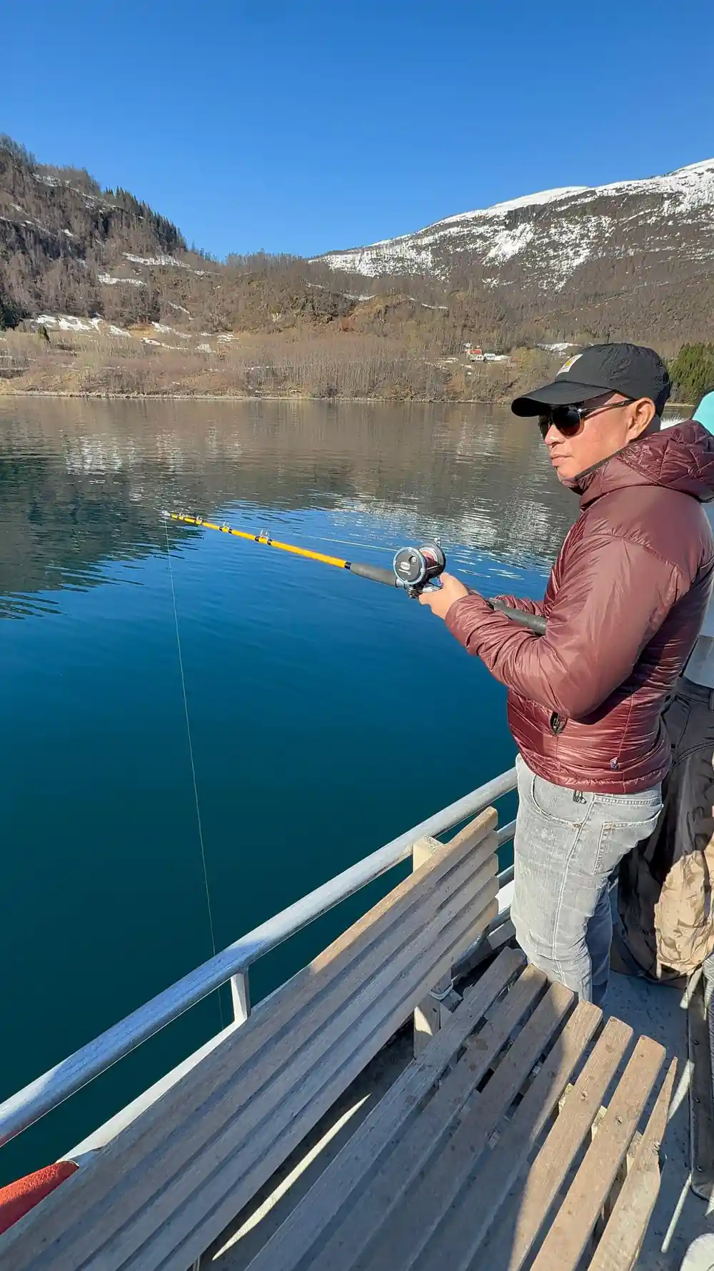 Man in burgundy jacket fishing from boat railing