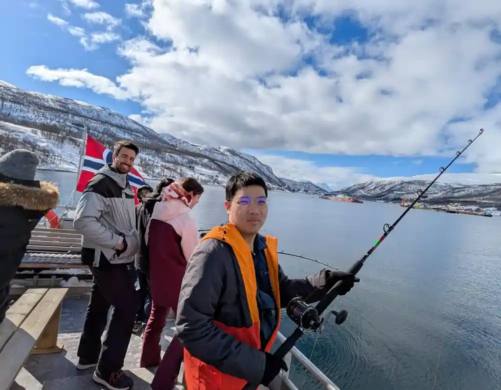 Man fishing on boat with Norwegian flag and mountains