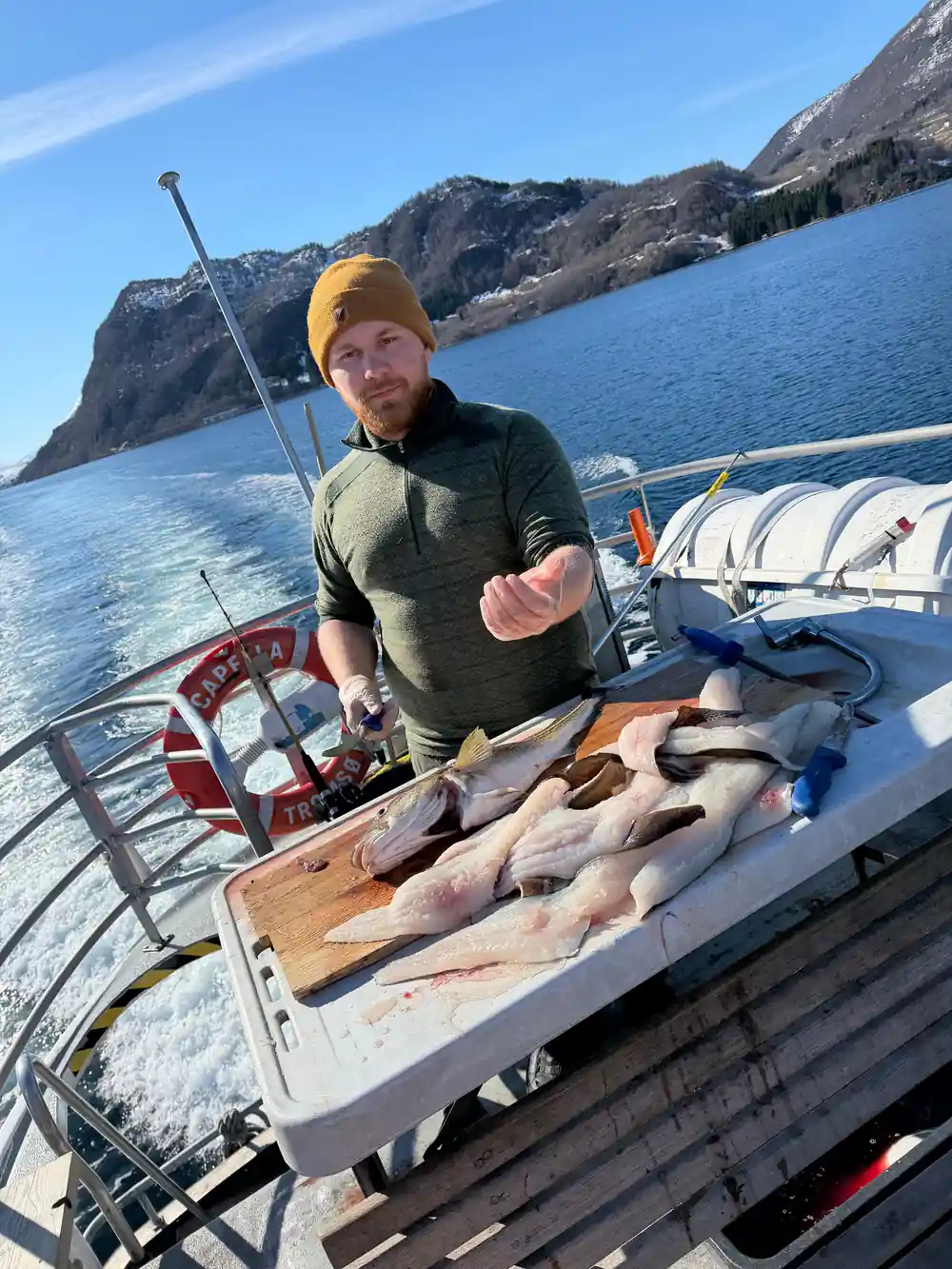 Man holding caught fish on boat with mountain backdrop