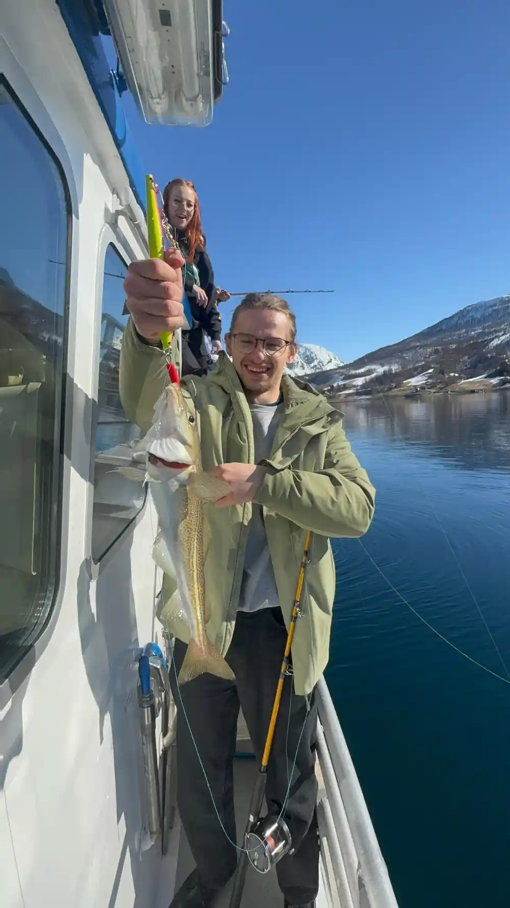 Man holding large fish on boat by mountain lake