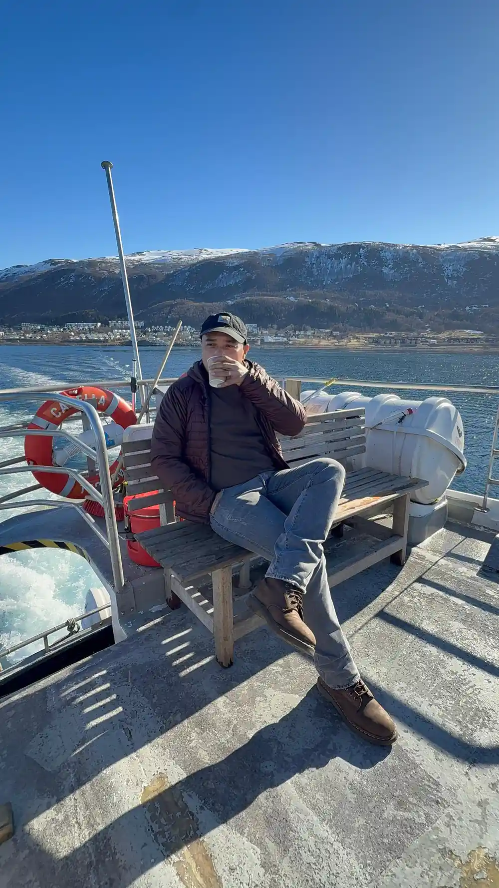 Man sitting on boat with snowy mountains behind