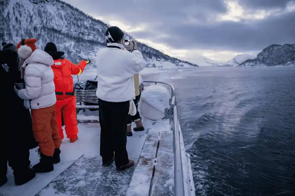 Passengers on boat deck with snowy mountains across fjord