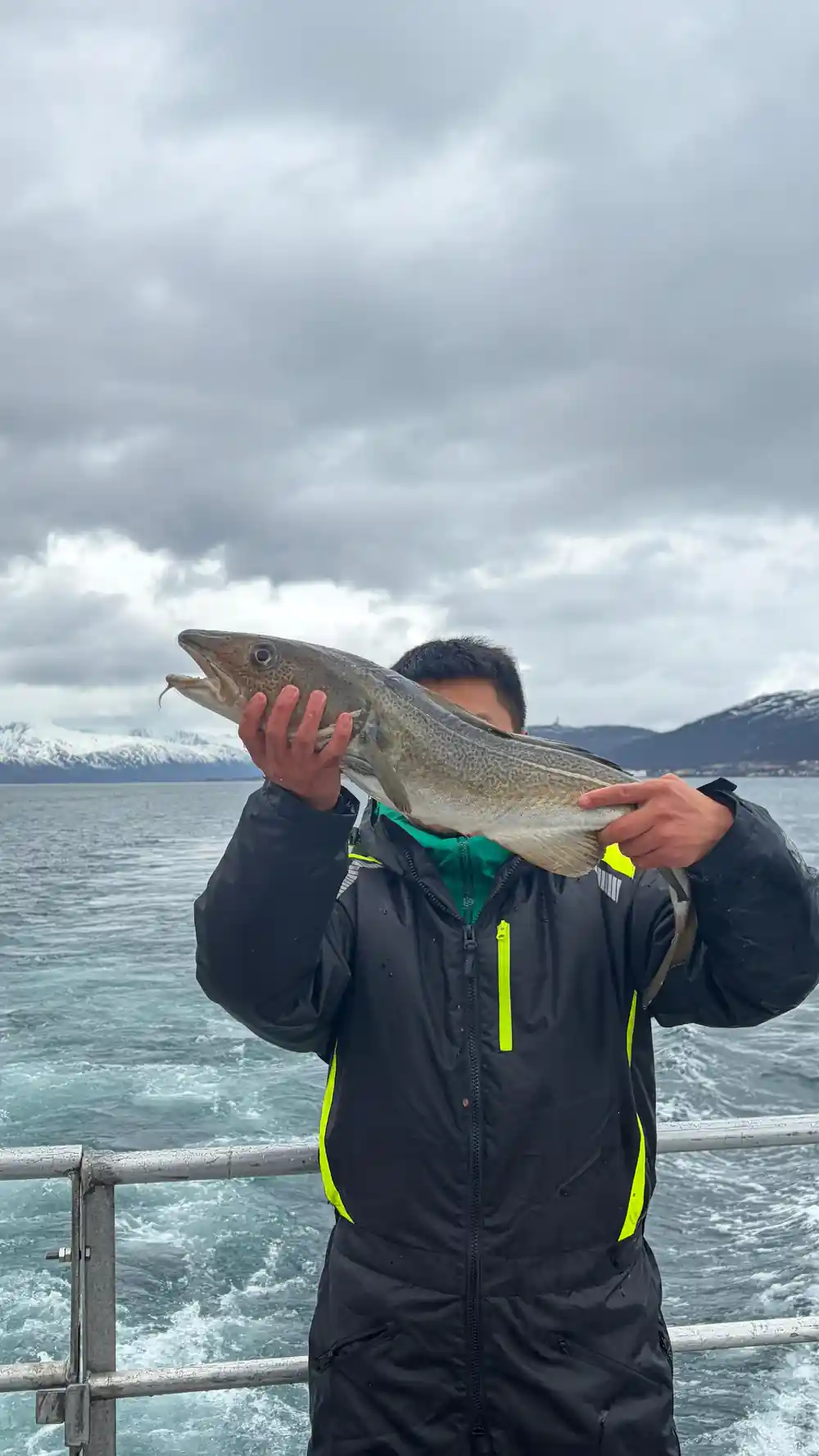 Person holding caught fish on boat in jacket