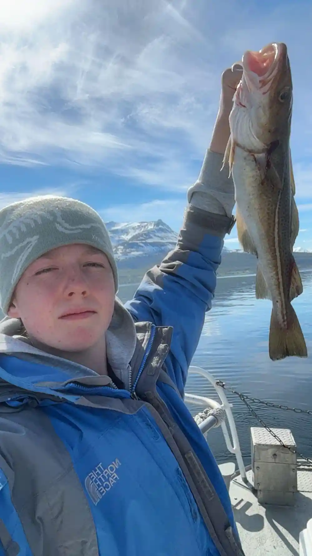 Person holding large fish against snowy mountain lake