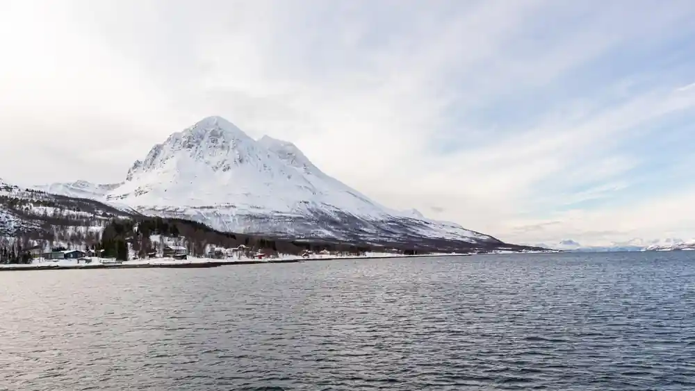 Snow-capped conical mountain across calm water