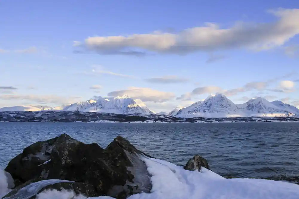 Snow-covered rocky peaks with fjord and mountains beyond
