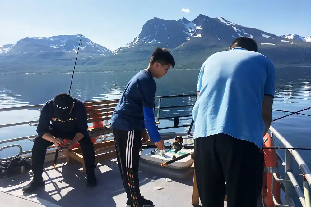 Three people on boat deck with snow mountains in background