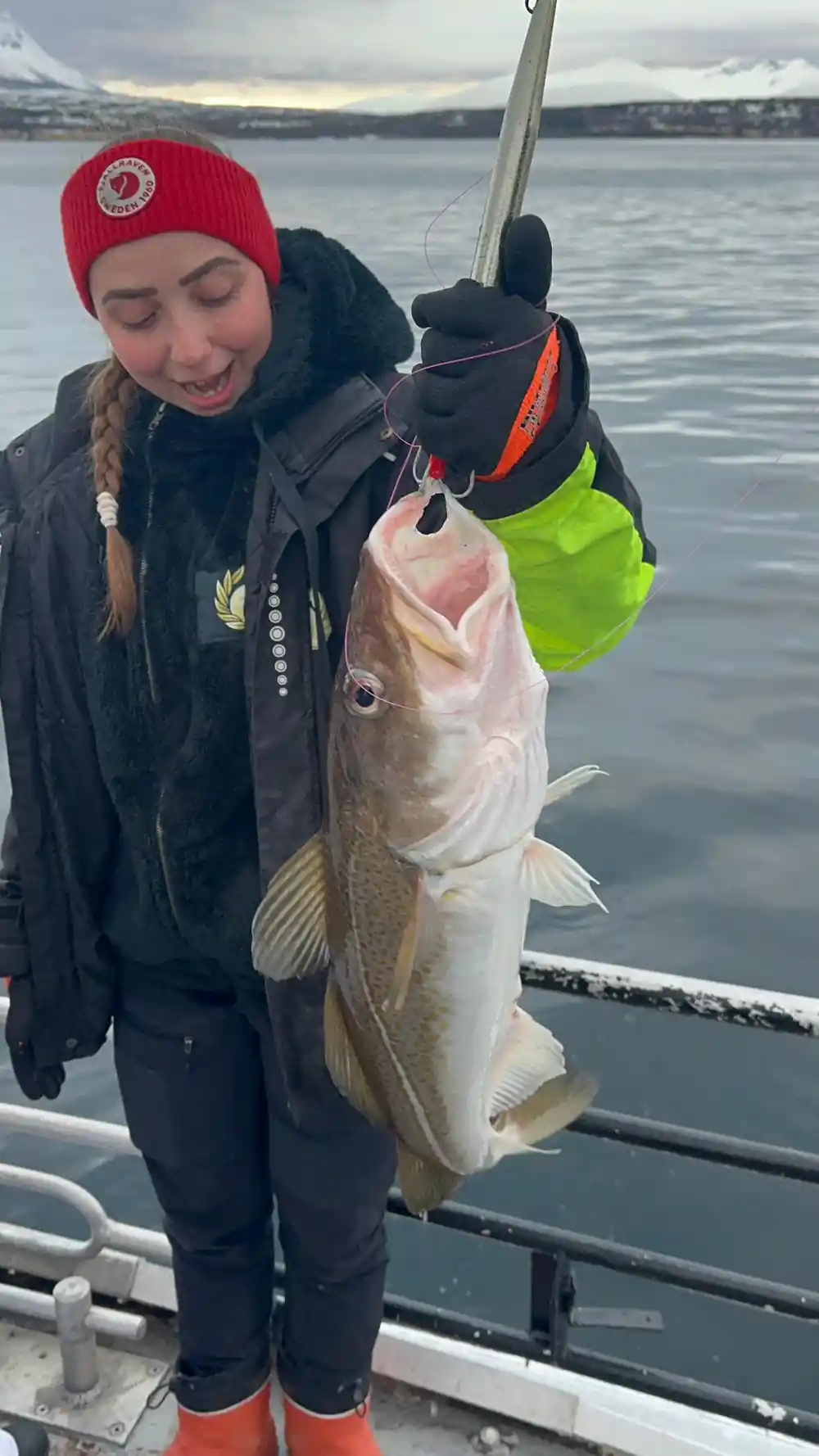 Three people on boat holding large fish, sunny