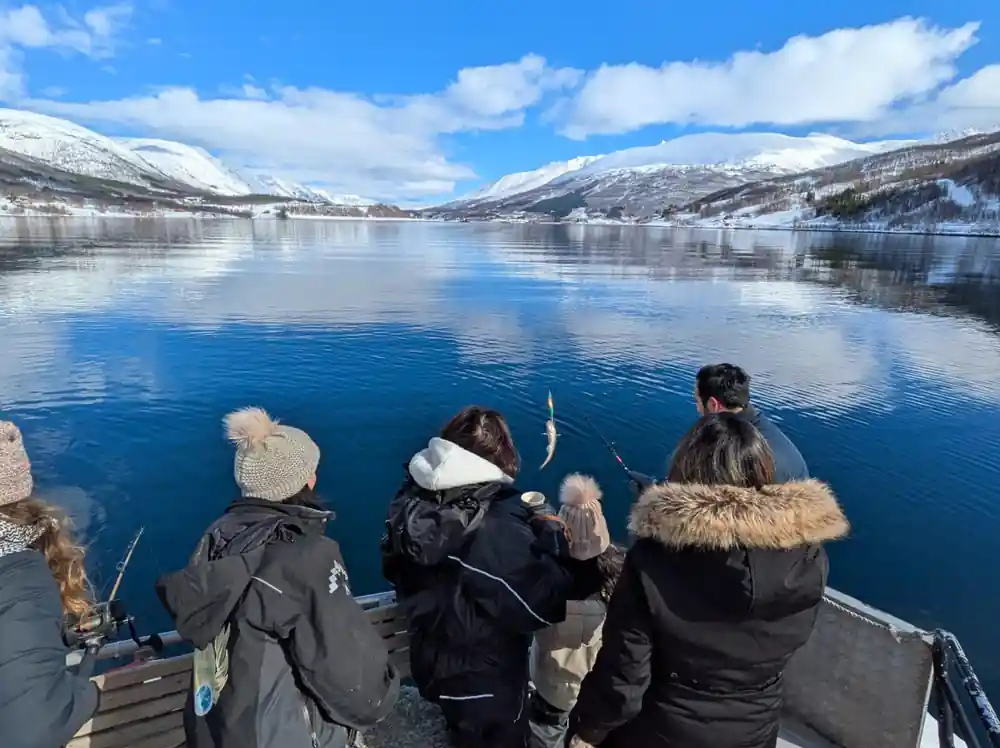 Three people viewing blue lake with snowy mountains