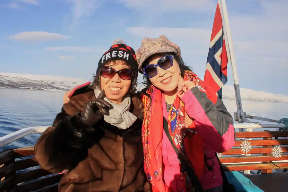 Two women on boat with Norwegian flag and snowy mountains