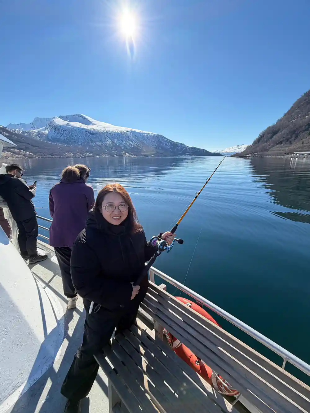 Woman fishing on boat with snowy mountain backdrop