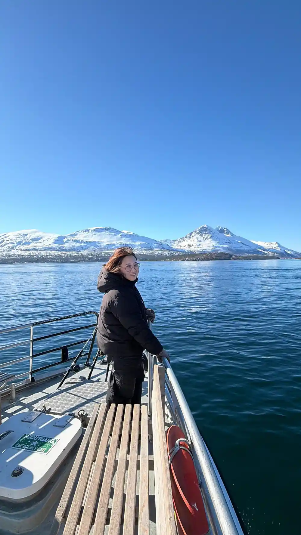Woman standing on boat deck with snowy peaks ahead