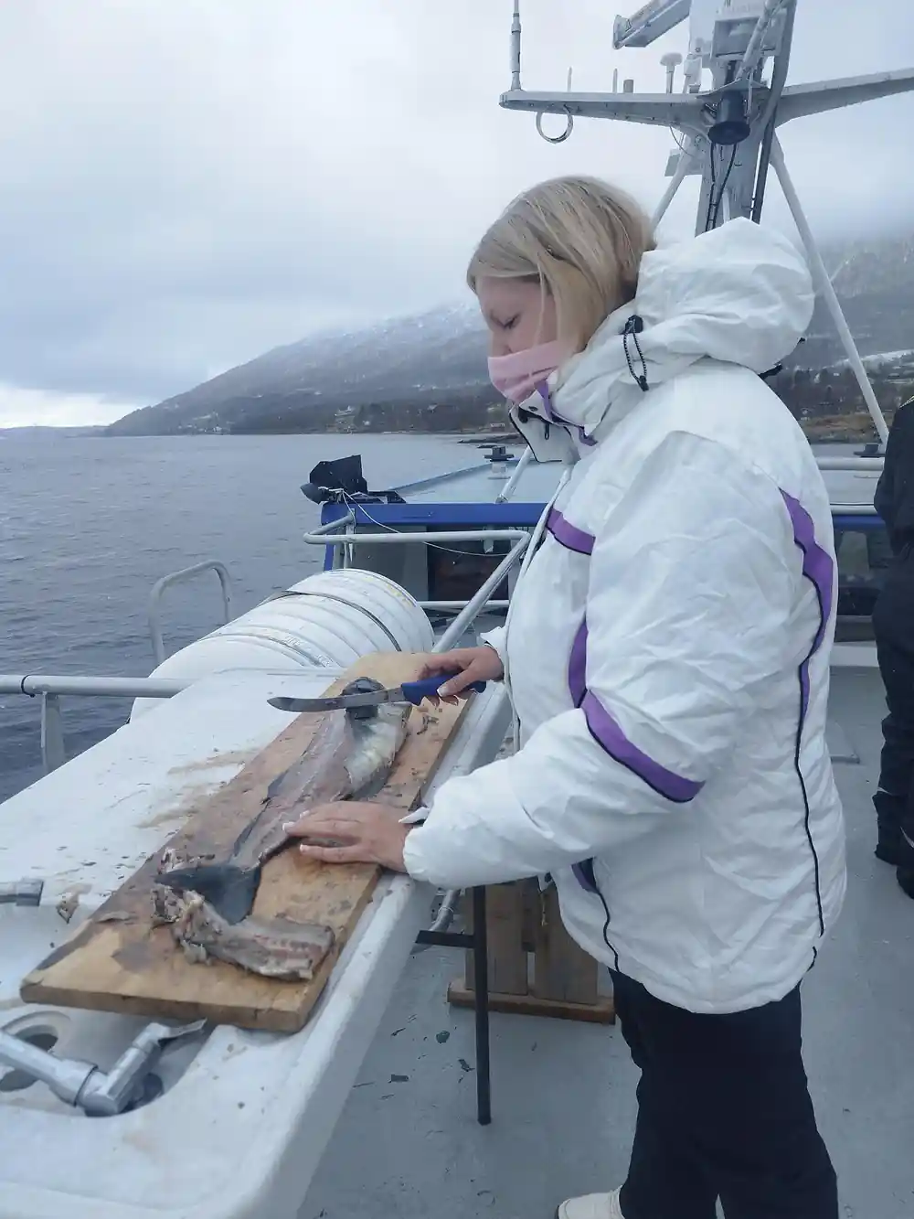 Woman in white jacket cleaning fish on boat